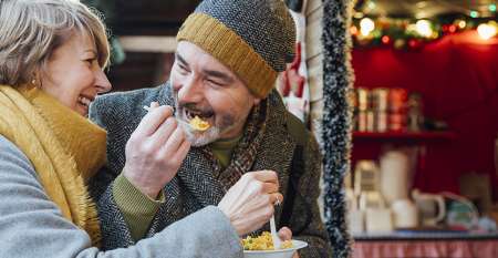 Mature couple sharing food at Christmas market stall