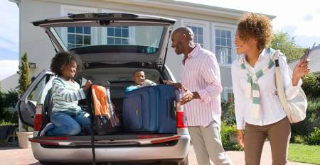 Parents smiling at children with suitcases in boot of car