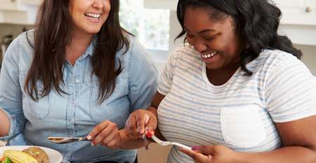 Two happy women eating in kitchen