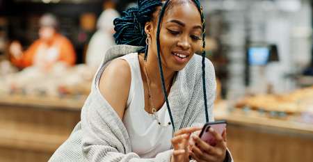 Young woman leaning over shopping trolley using mobile phone