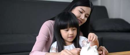 Financial concepts. The mother is teaching her daughter to know how to drop the piggy bank.