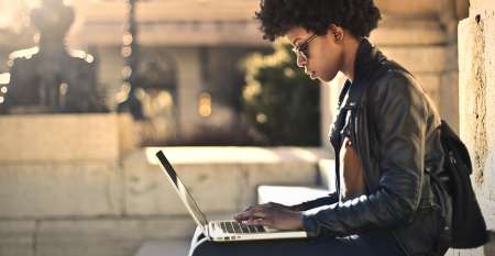 Young woman sitting on step outdoors using laptop