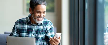 Man smiling looking mobile phone with laptop