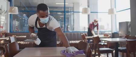 Man wearing medical mask cleaning table